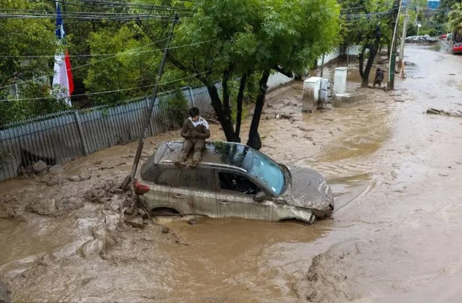 Una persona se resguarda sobre un vehículo afectado por un aluvión este jueves, en la comuna de Las Condes, en Santiago (Chile). Las autoridades chilenas informaron que, en medio de las fuertes lluvias que afectan la zona centro-sur del país, se produjo un aluvión en una zona precordillerana en el este de Santiago, que arrastró vehículos y buses. EFE - Javier Torres